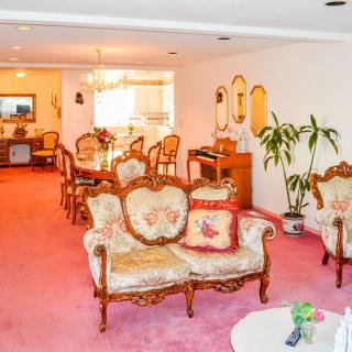 A spacious living and dining area featuring vintage furniture with a pink carpet and elegant decor.