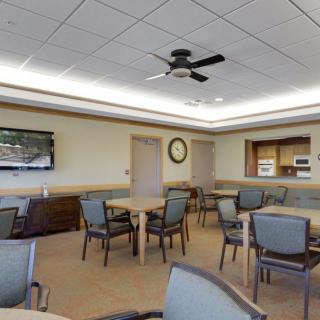 A spacious dining room with tables and chairs, featuring a television, ceiling fan, and wall clock.