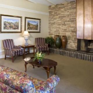 A cozy living room with vintage furniture and a brick fireplace, featuring two armchairs, a floral sofa, and decorative vases.