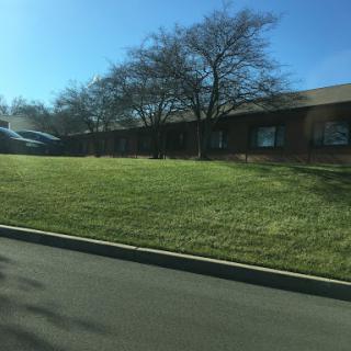 A peaceful scene featuring a grassy area in front of a building, framed by trees under a clear blue sky.