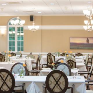 An elegant dining room with neatly arranged tables and chairs, adorned with chandeliers.