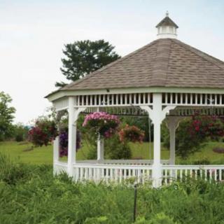 A picturesque white gazebo surrounded by lush green vegetation and hanging flowers in a garden setting.