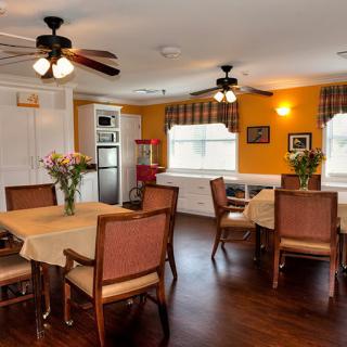 A cozy dining room with tables and chairs, adorned with vases of flowers and lit by ceiling fans.