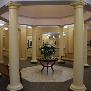 A well-lit lobby area featuring elegant columns and a central table with floral arrangements.