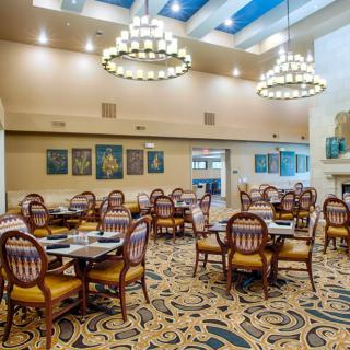 An elegant dining room with ornate chairs and tables, featuring chandeliers and wall paintings.