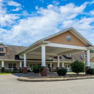 A large building with a covered entrance and landscaped surroundings under a partly cloudy sky.