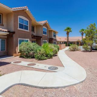 A row of residential apartments with a landscaped walkway surrounded by desert plants and palm trees on a sunny day.