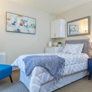 A modern bedroom with a single bed adorned with a geometric-patterned comforter and a blue throw, complemented by a blue chair and artistic wall decor.
