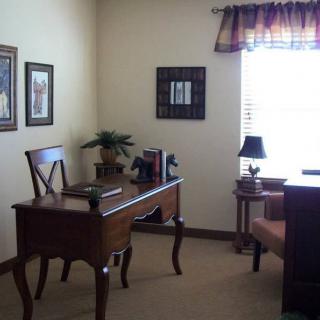 A small, neatly arranged office space with a wooden desk and chair, adorned with books and decorative elements near a window that lets in natural light.