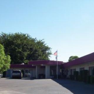A small motel with a parking lot and an American flag flying under a clear blue sky.