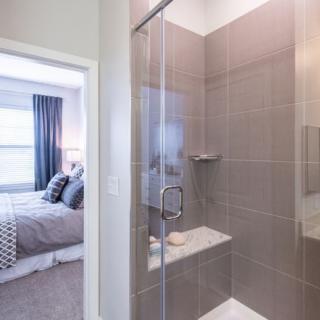 Modern bathroom with a glass shower next to a cozy bedroom.