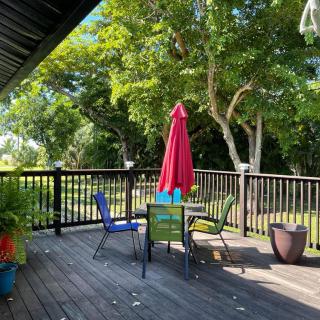 A peaceful outdoor deck with a table, chairs, and a red umbrella surrounded by trees.