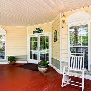 A welcoming porch with a rocking chair and potted plants, leading to the entrance of a house.