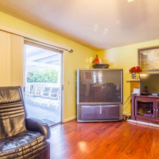 A cozy living room featuring a large television, leather chair, and fireplace, with hardwood flooring and a sliding glass door leading outside.