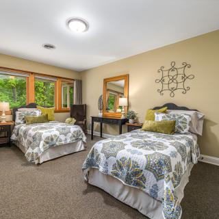 A cozy bedroom featuring twin beds with matching decor and ample natural light from large windows.