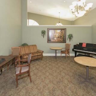 A cozy room with a piano, sofa, tables, and chairs under a chandelier.