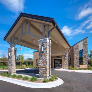 A modern hospitality building featuring a welcoming entrance with stone accents and well-maintained landscaping under a clear blue sky.