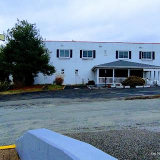 A view of a two-story commercial building under a cloudy sky, featuring an entrance and parking area.