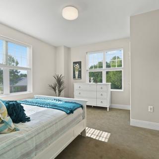 A bright and modern bedroom with white furniture and large windows letting in natural light.