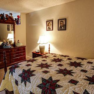 A cozy bedroom with a star-patterned quilt on the bed and warm lighting from a bedside lamp, adorned with family photographs and wooden furniture.
