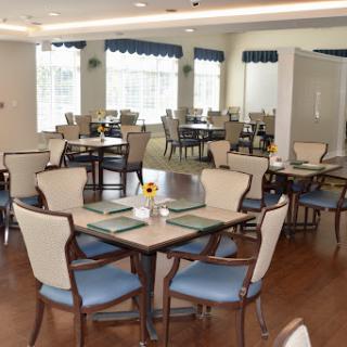 A spacious and elegantly designed dining area featuring neatly arranged tables and comfortable chairs, illuminated by natural light.
