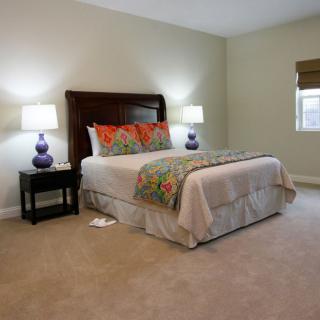 A cozy bedroom with a neatly made bed, flanked by nightstands and lamps, in soft neutral tones.
