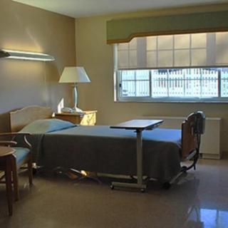 An empty hospital room with a single bed and a window allowing natural light in.