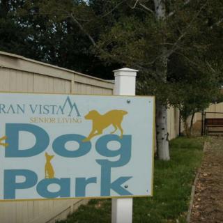 Sign for a dog park next to a fenced area with trees.