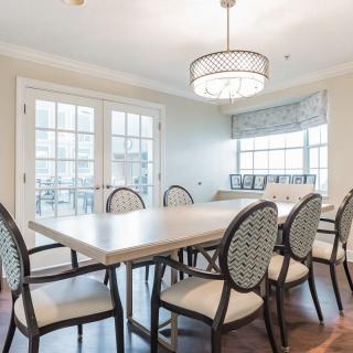 A well-lit dining room featuring a large table surrounded by elegant chairs, with a modern chandelier and large windows providing natural light.