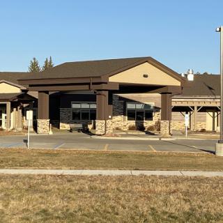 A modern commercial building with a welcoming entrance, surrounded by grass under a clear blue sky.