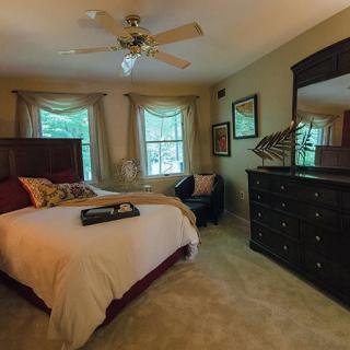 A cozy bedroom with a comfortable bed, dresser, and mirror, featuring a ceiling fan and large windows.