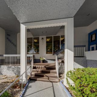 The image shows the entrance of a building with stairs leading up, surrounded by railings and plants.