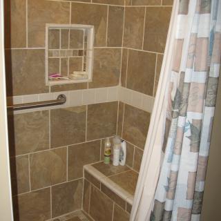 A tiled shower with a corner shelf and curtain.