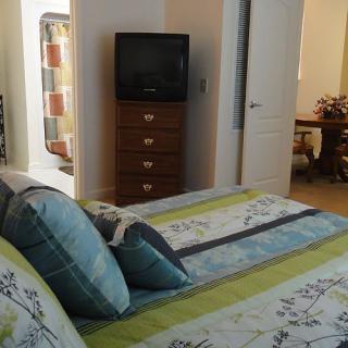 A cozy bedroom featuring a neatly made bed, a television on a dresser, and an open doorway.