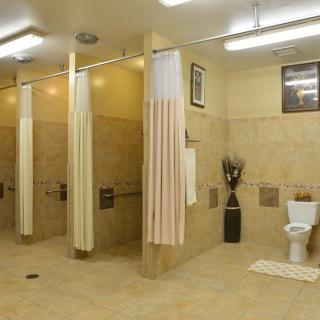 A tiled bathroom with shower stalls, curtains, and a toilet.