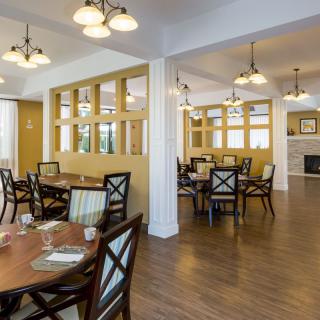 A cozy dining room with neatly arranged tables and chairs, illuminated by elegant lighting fixtures.