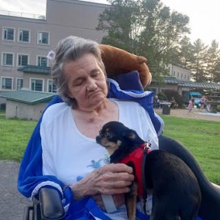 An elderly woman enjoys a moment of affection with her small Chihuahua in a park.
