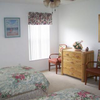 A cozy bedroom with two beds, a wooden dresser, and a window adorned with floral curtains.