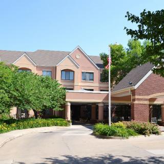 A large brick building with a main entrance surrounded by trees and a circular driveway.