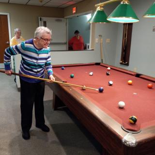 An elderly man playing billiards in a game room.