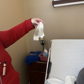 A person in red is holding a gown next to a hospital bed.