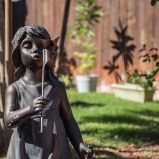 A garden sculpture of a girl holding a flower under sunlight.