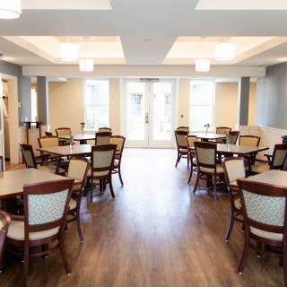 An elegant dining room with multiple tables and chairs, featuring wood flooring and soft lighting.