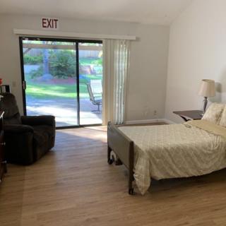 A cozy bedroom with a bed, armchair, and sliding glass doors opening to a garden view.