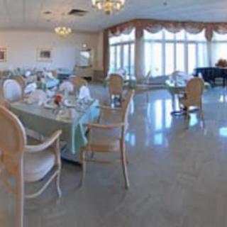 An elegant dining room with neatly arranged tables and chairs, featuring chandeliers and large windows.