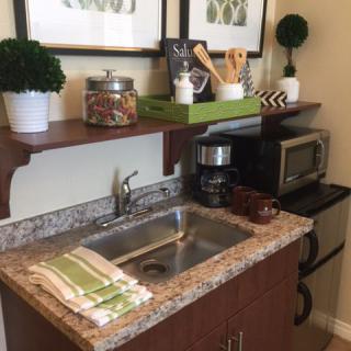 A compact kitchen setup with a sink, coffee maker, and microwave, decorated with plants and jars.