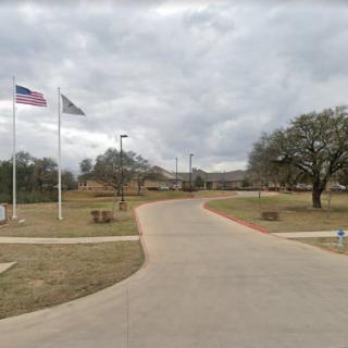A paved road leading to a building with flags and trees under a cloudy sky.