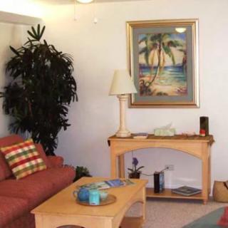 A cozy living room featuring a sofa, coffee table, and a decorative painting of palm trees.