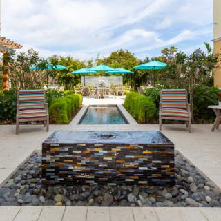 A serene outdoor patio area featuring a decorative fountain, surrounded by lounge chairs and umbrellas in a lush garden setting.