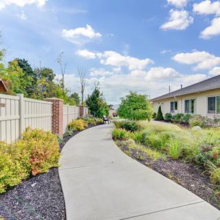 A peaceful residential pathway lined with gardens and fences under a partly cloudy sky.